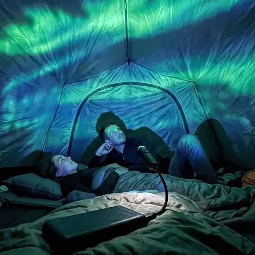 Groen en blauw noorderlicht geprojecteerd op een tentdoek bij nacht